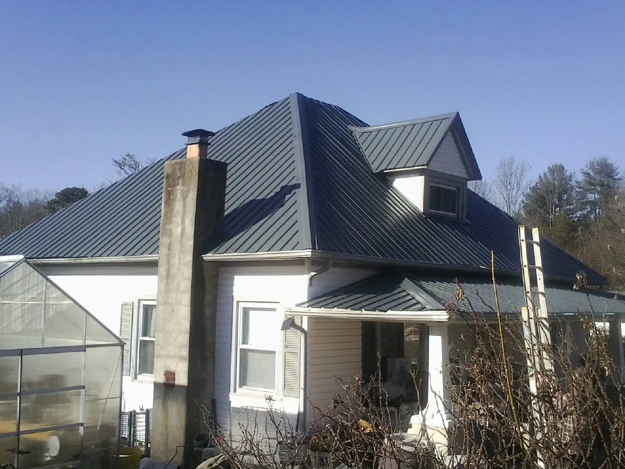 Dark blue standing seam metal roof on a white farmhouse with dormer — Slate & Tile Roof Repair by Roofing Brothers in Averill Park