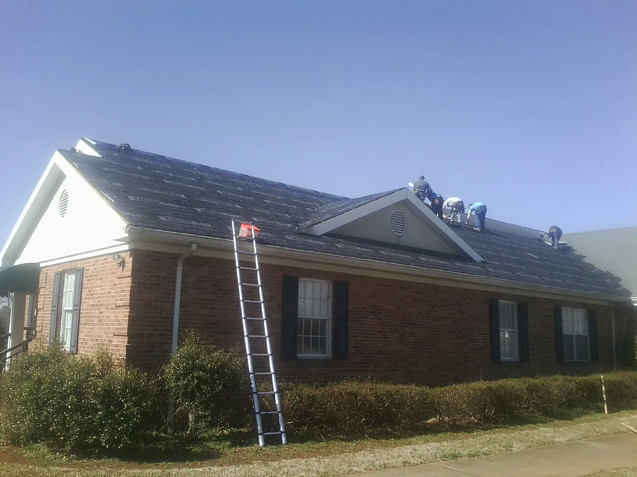 Crew tearing shingles off a brick ranch roof with a ladder set — Emergency Roof Repair work by our crew in Averill Park