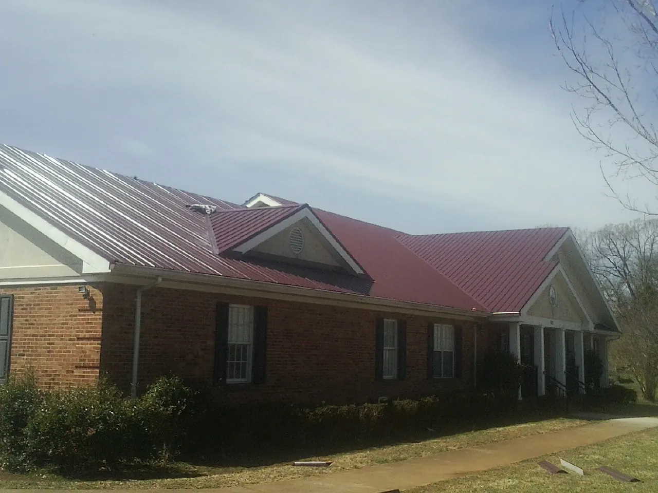 Red metal roof with gabled entries on a long brick building, from a Hail Damage Roof Repair job in Averill Park