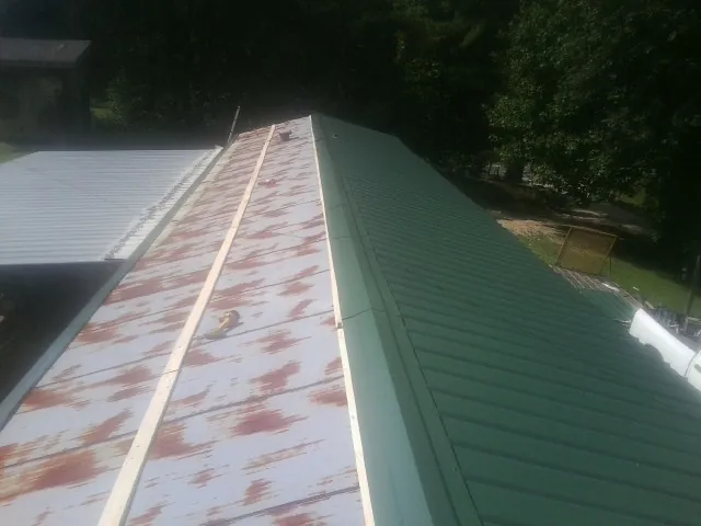 Old rusted panels beside newly installed green metal roofing — Wind Damage Roof Repair by Roofing Brothers in Averill Park