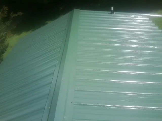 New green metal panels meeting at the ridge of a roof — Flat Roof Repair work by our crew in Averill Park