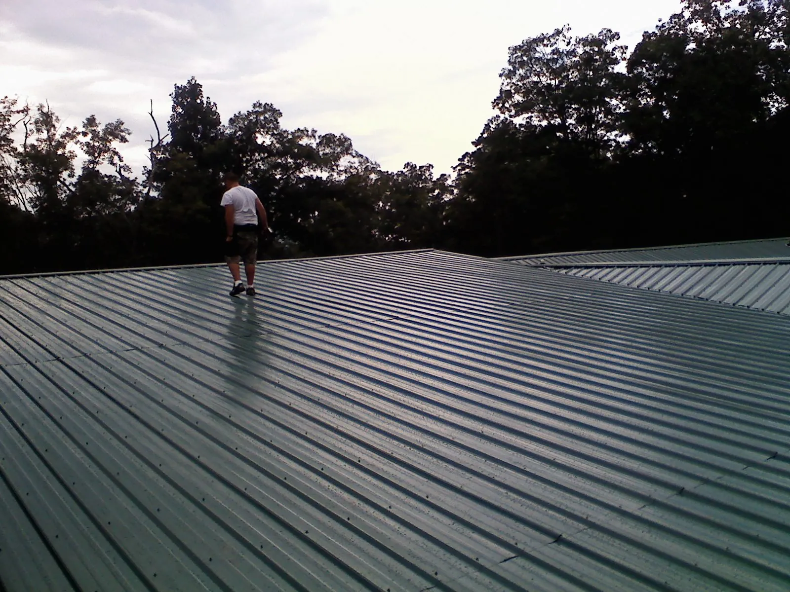 Roofer walking a wide expanse of new green metal roofing in Averill Park