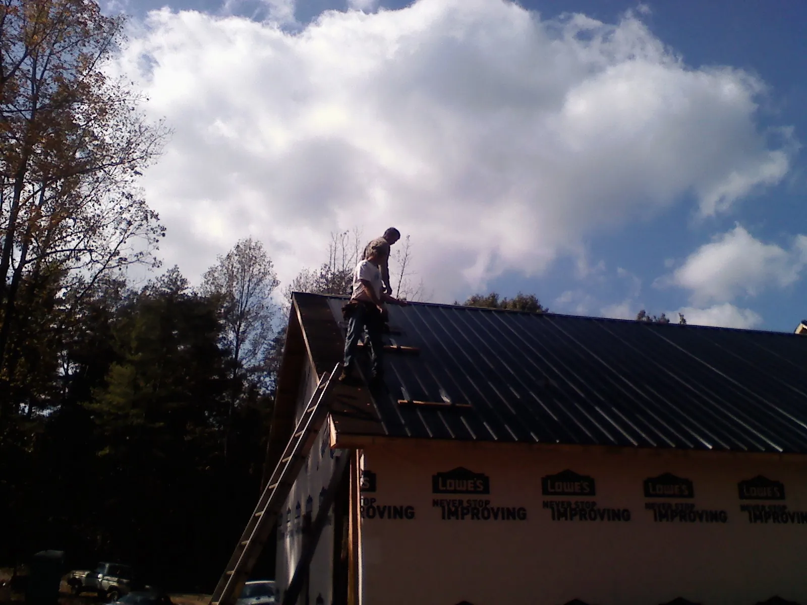 Roofer fastening dark metal panels high against a cloudy sky, from a Roof Inspection job in Averill Park