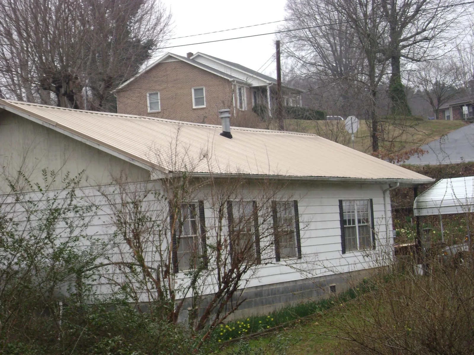Tan metal roof on a white sided house set into a hillside — Commercial Roofing by Roofing Brothers in Averill Park