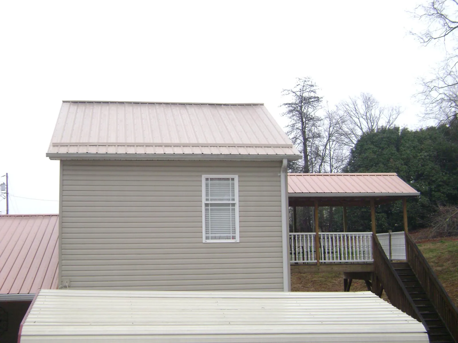 Tan metal roofs on a two story addition and attached porch, from a Roof Replacement job in Averill Park